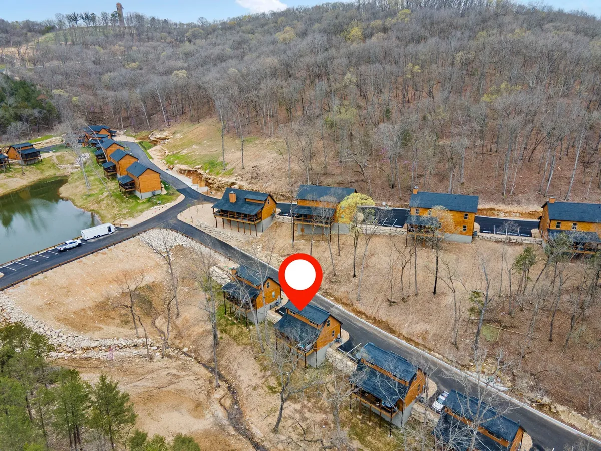 A panoramic view of Tall Timbers Camp’s environment, showcasing wooden cabins nestled among trees, a scenic pond, and a winding road. The tranquil setting is ideal for hiking, fishing, and family gatherings, demonstrating the natural beauty and range of outdoor activities available.