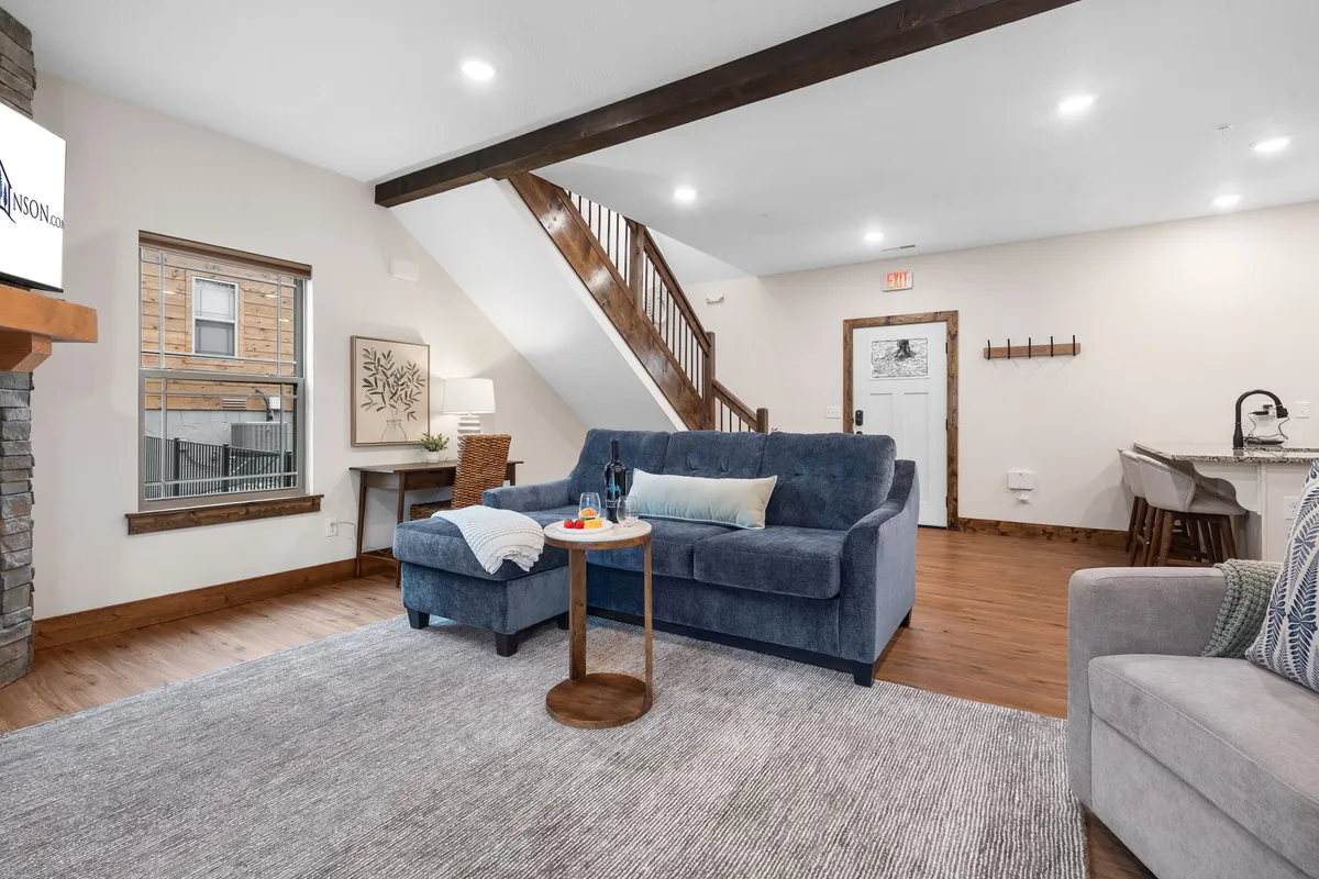 A comfortable living room featuring a plush sofa, stylish coffee table, artwork on the wall, and a staircase in view. The room feels inviting and designed for relaxation, socializing, or quiet moments with loved ones.