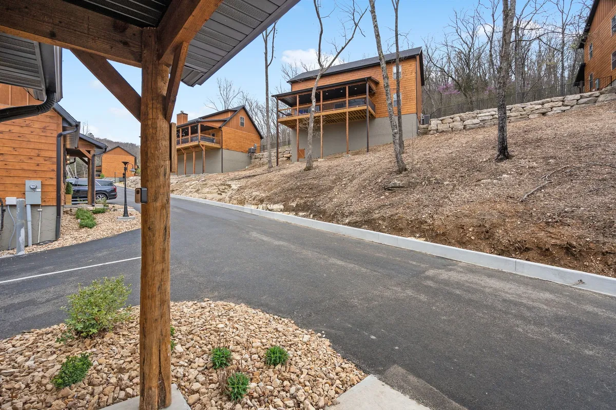 Wooden cabins line a paved driveway, set amid a landscaped green area with benches and trees. The peaceful setting offers opportunities for relaxing strolls and quiet moments outdoors.