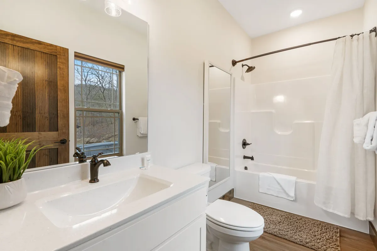 A bright bathroom interior featuring a sink, large mirror, shower area, and a window letting in ample daylight. The space feels inviting and serene, ideal for personal routines and relaxation.
