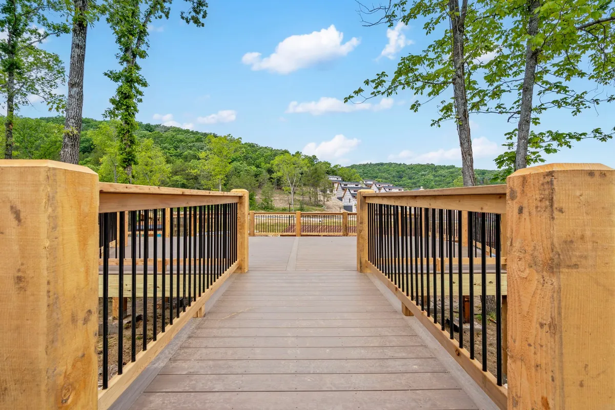 A serene exterior scene featuring a rustic wooden bridge surrounded by lush trees and rolling hills in the background. The area looks peaceful and inviting for walking and enjoying nature.