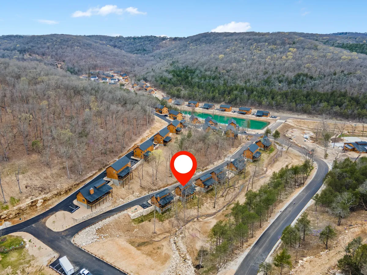 This image captures wooden cabins nestled among scattered trees and a winding road, with the majestic Ozark mountains in the background. The warm, natural light and relaxed outdoor setting evoke a sense of peace and adventure, inviting guests to imagine themselves hiking or exploring the nearby trails.