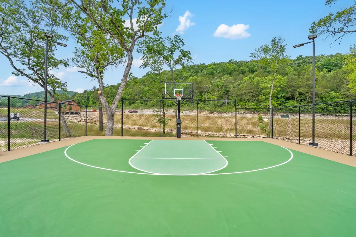 An outdoor basketball court nestled among green trees, featuring a basketball hoop and fence. The scene is energetic, inviting guests to enjoy friendly matches and active recreation in a natural setting.