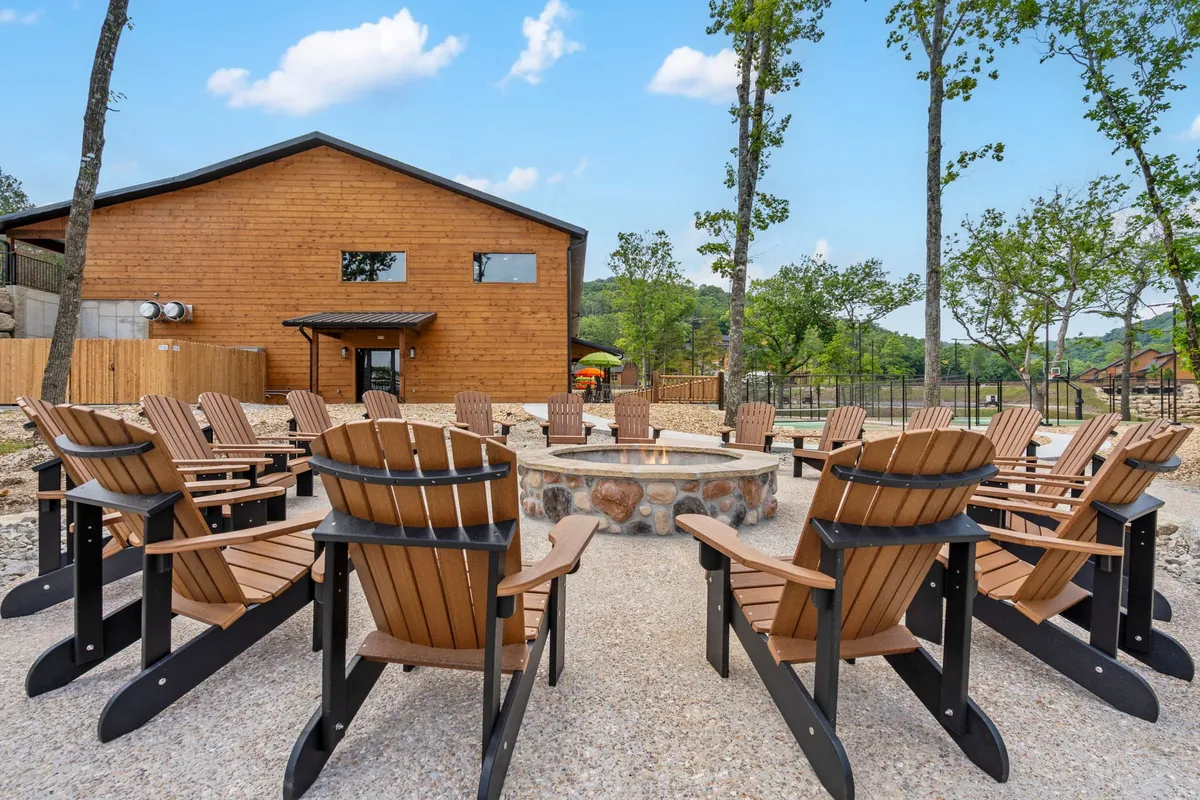 A rustic fire pit surrounded by Adirondack chairs sits on a wooden deck next to a cabin structure. The scene is perfect for evening gatherings, storytelling, or relaxing under the stars, with visible natural surroundings enhancing the ambiance.