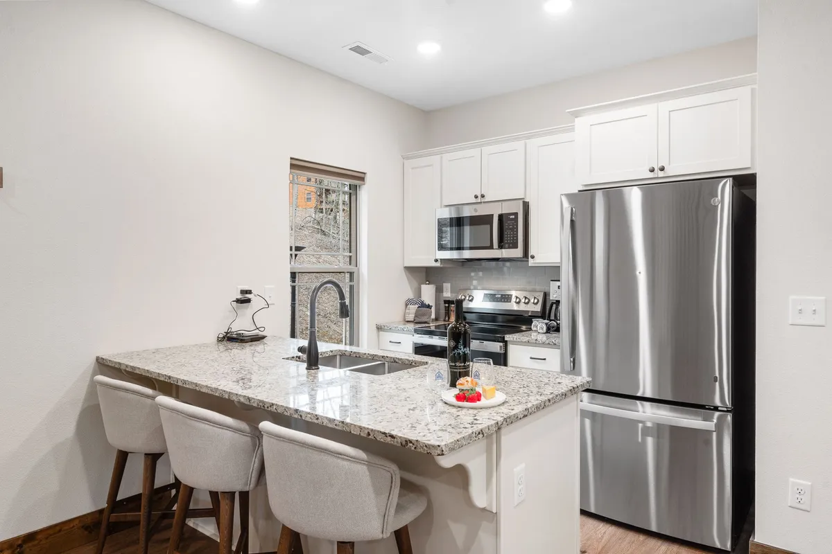 A bright kitchen area with a sleek granite countertop, stainless steel appliances, bar stools for casual dining, and a window that lets nature in. The setup suggests a chef-ready kitchen ideal for preparing family meals or hosting friends.